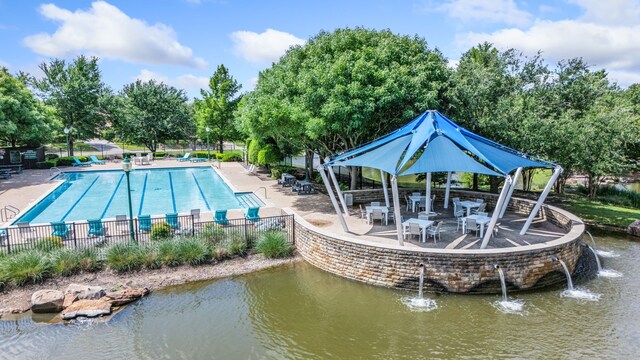 community pool featuring fence, a gazebo, a patio area, view of wooded area, and a water view