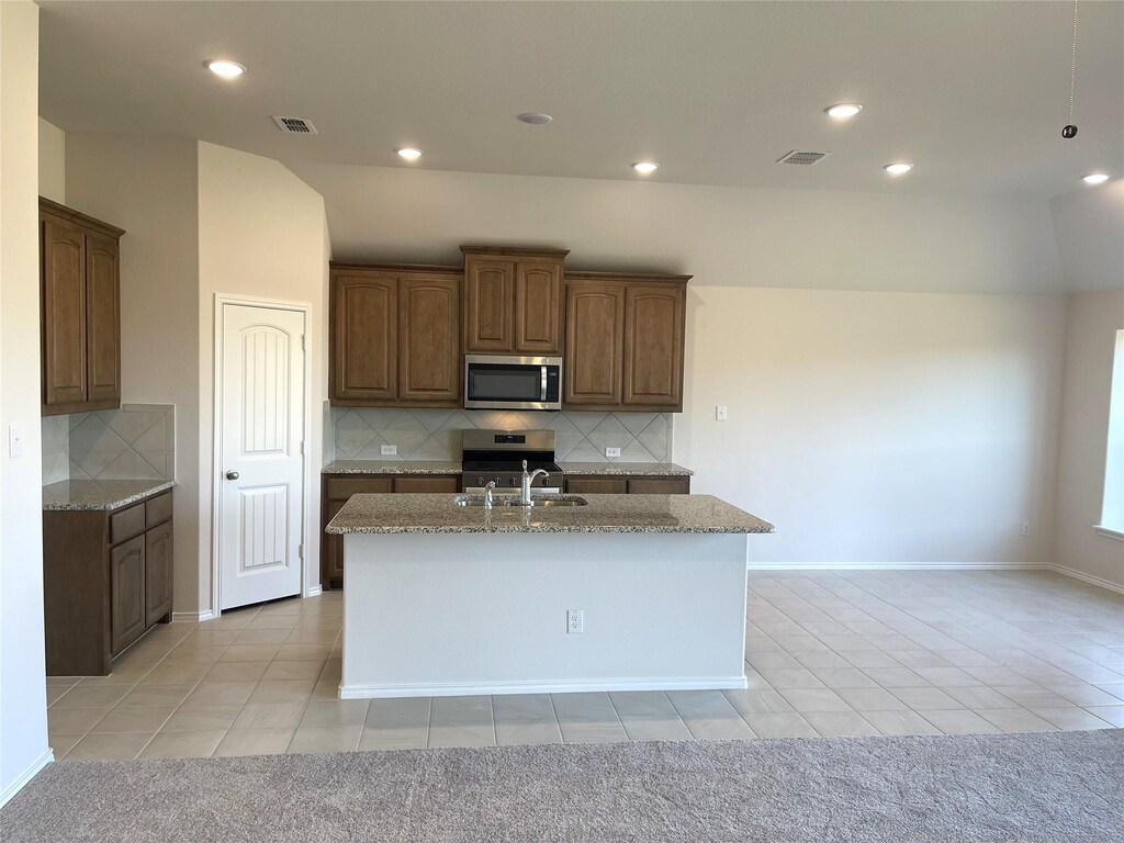 kitchen featuring tasteful backsplash, light tile patterned floors, stainless steel appliances, and a kitchen island with sink