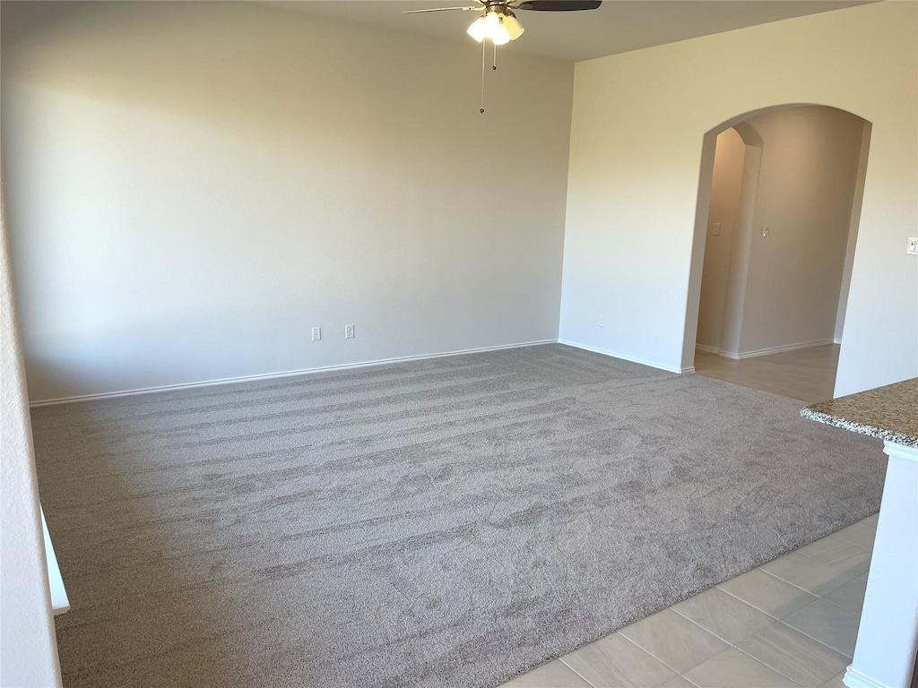 empty room featuring arched walkways, a ceiling fan, light colored carpet, and baseboards