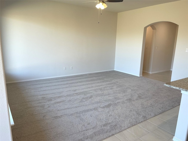 empty room featuring arched walkways, a ceiling fan, light colored carpet, and baseboards