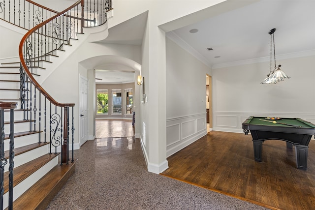 foyer entrance with crown molding, arched walkways, wainscoting, stairs, and baseboards