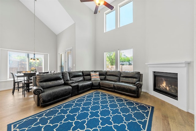 living area featuring a wealth of natural light, high vaulted ceiling, wood finished floors, and ceiling fan with notable chandelier