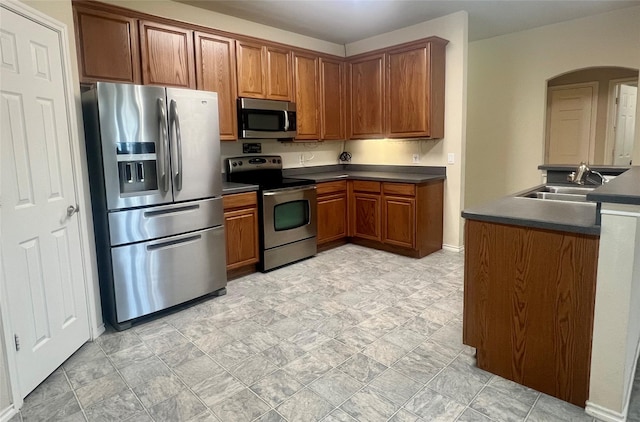 112 Jimmie Birdwell Blvd, Ferris, TX 75125 - kitchen featuring dark countertops, a sink, brown cabinets, arched walkways, and stainless steel appliances