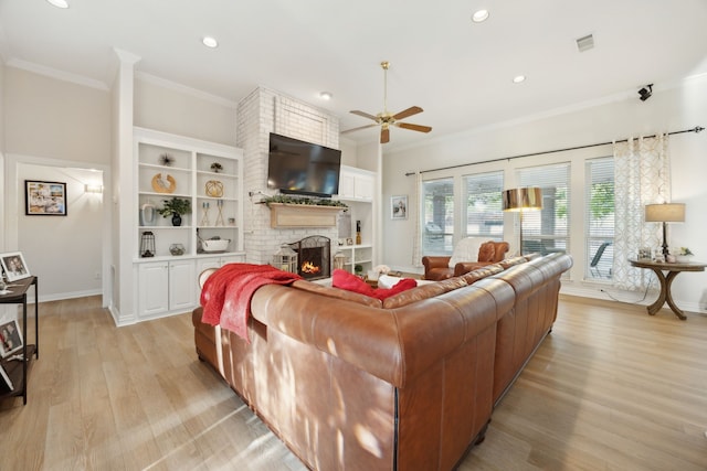 living area with crown molding, light wood-style floors, ceiling fan, a fireplace, and visible vents
