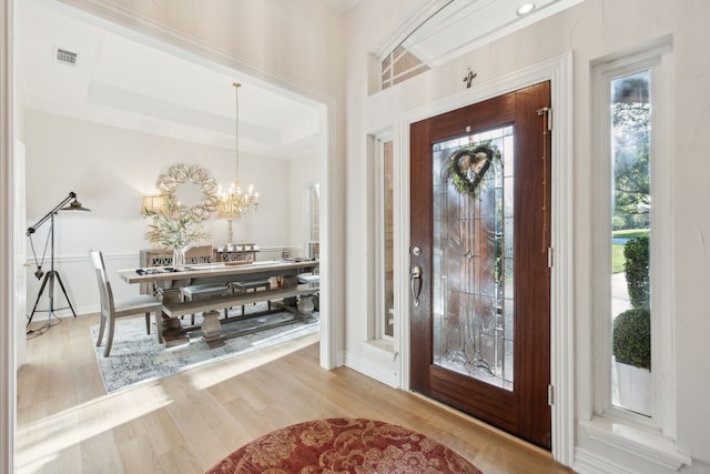 entrance foyer with a chandelier, a raised ceiling, visible vents, and wood finished floors