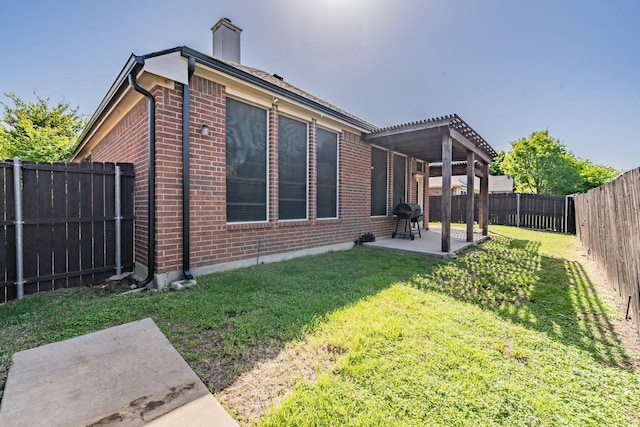 back of house with a yard, a patio area, a chimney, a fenced backyard, and brick siding