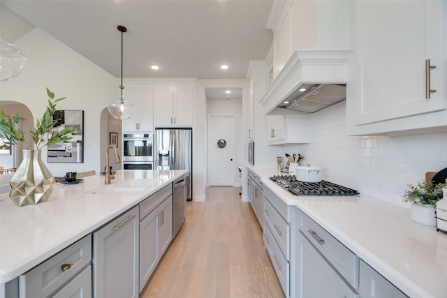 3101 Twin Eagles Dr, Celina, TX 75009 - kitchen with premium range hood, stainless steel appliances, arched walkways, light wood finished floors, and a sink