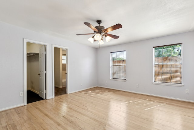 unfurnished bedroom featuring ensuite bathroom, light wood-type flooring, a walk in closet, and baseboards