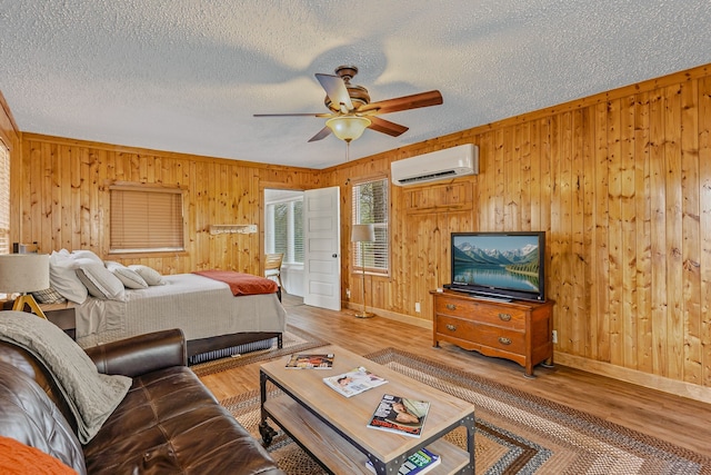 bedroom with a wall mounted air conditioner, wood walls, a textured ceiling, and wood finished floors