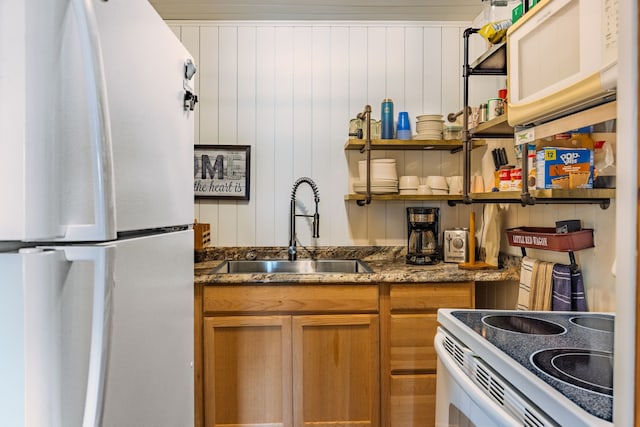 kitchen featuring dark stone countertops, open shelves, a sink, white appliances, and brown cabinets