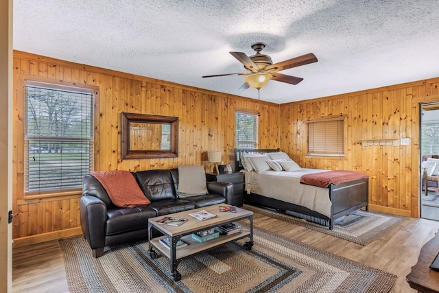 bedroom with a textured ceiling, wood finished floors, wooden walls, and baseboards