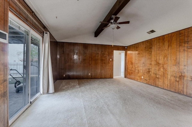 empty room with lofted ceiling with beams, carpet flooring, a ceiling fan, wood walls, and visible vents