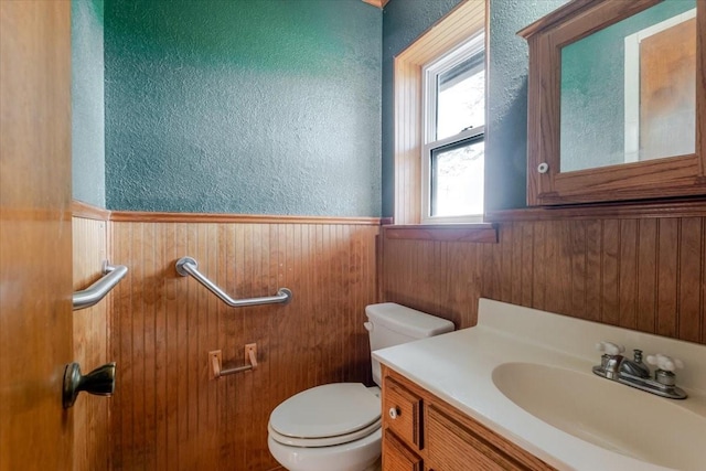 bathroom with toilet, a textured wall, wainscoting, vanity, and wood walls