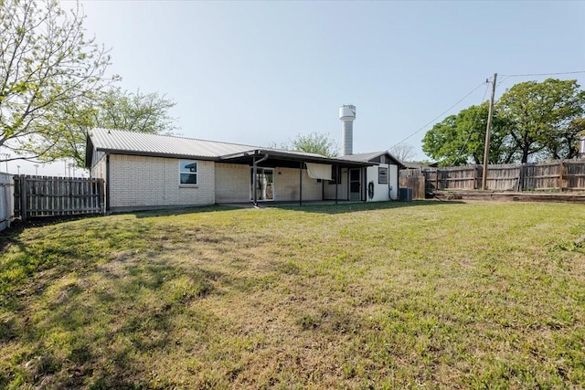rear view of property with a fenced backyard, central AC unit, metal roof, and a lawn