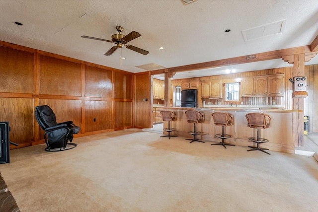 interior space with ceiling fan, a textured ceiling, wooden walls, beamed ceiling, and light carpet