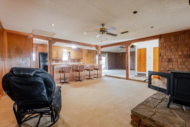 living room with wood walls, a wood stove, a ceiling fan, and a textured ceiling