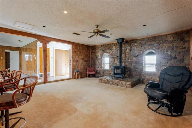 sitting room featuring a wood stove, carpet, a textured ceiling, and a ceiling fan