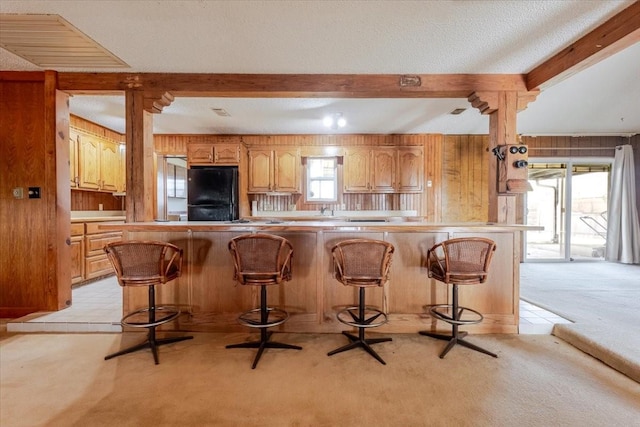 kitchen with wooden walls, beam ceiling, freestanding refrigerator, and light carpet
