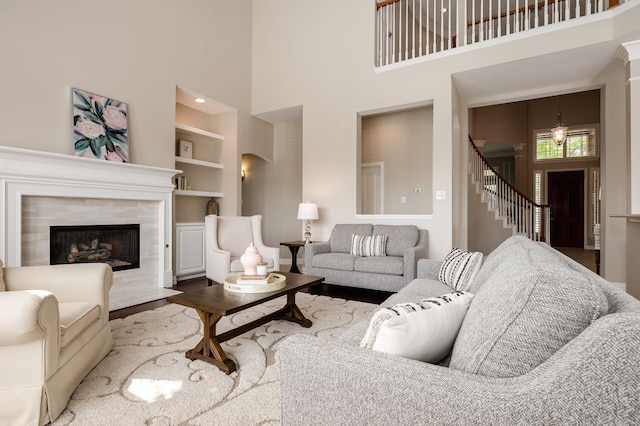 living room featuring a towering ceiling, built in shelves, wood finished floors, stairs, and a tile fireplace