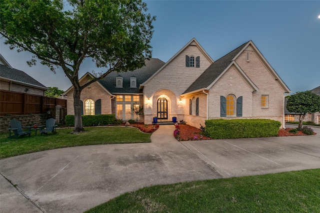 view of front of home with roof with shingles, brick siding, fence, and a front lawn