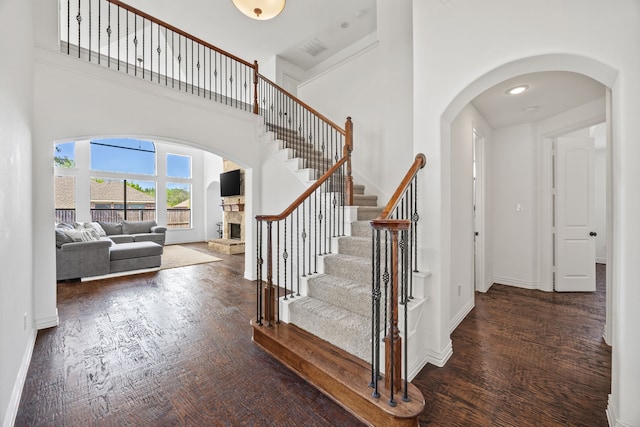4504 Oxbow Dr, Mckinney, TX 75072 - stairway with wood finished floors, a towering ceiling, a fireplace, arched walkways, and baseboards