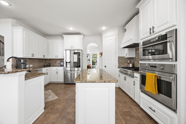 4504 Oxbow Dr, Mckinney, TX 75072 - kitchen featuring stainless steel appliances, arched walkways, premium range hood, backsplash, and a kitchen island