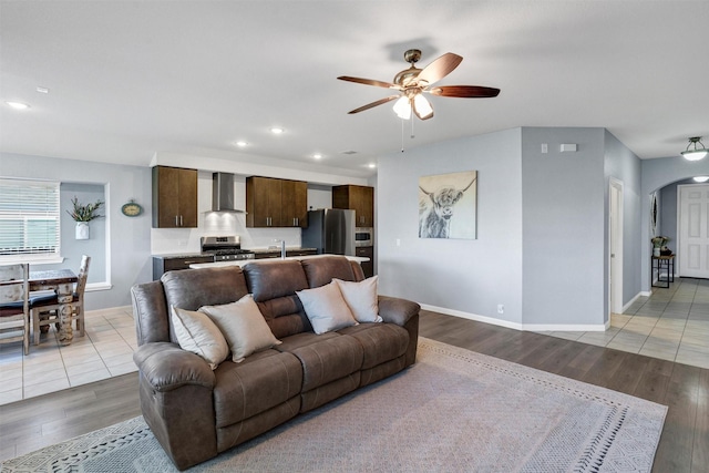 living room with arched walkways, light wood-type flooring, baseboards, and ceiling fan