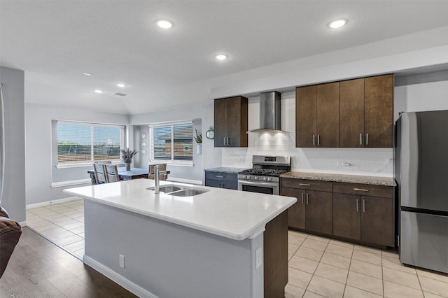 kitchen featuring wall chimney range hood, light countertops, a sink, and appliances with stainless steel finishes