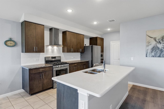 kitchen featuring freestanding refrigerator, wall chimney exhaust hood, visible vents, a sink, and stainless steel gas range oven