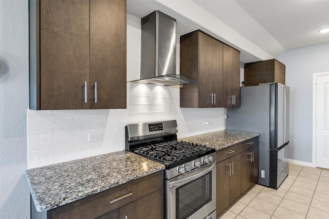 kitchen with dark stone countertops, wall chimney exhaust hood, dark brown cabinetry, stainless steel appliances, and decorative backsplash