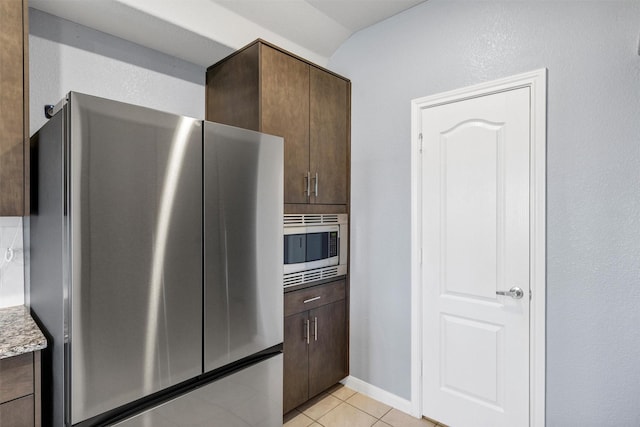 kitchen with stainless steel appliances, light stone countertops, dark brown cabinetry, and light tile patterned floors