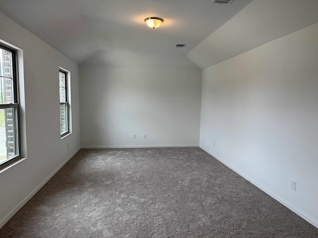 carpeted spare room featuring lofted ceiling and baseboards