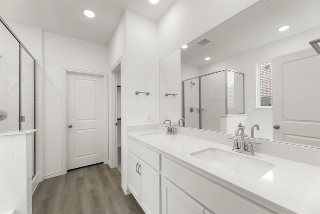 full bathroom featuring a shower stall, wood finished floors, double vanity, and recessed lighting