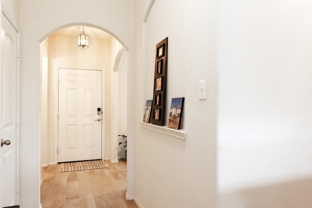 doorway featuring light wood-style flooring, baseboards, and arched walkways