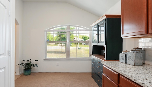 kitchen with light stone counters, vaulted ceiling, a wealth of natural light, and carpet