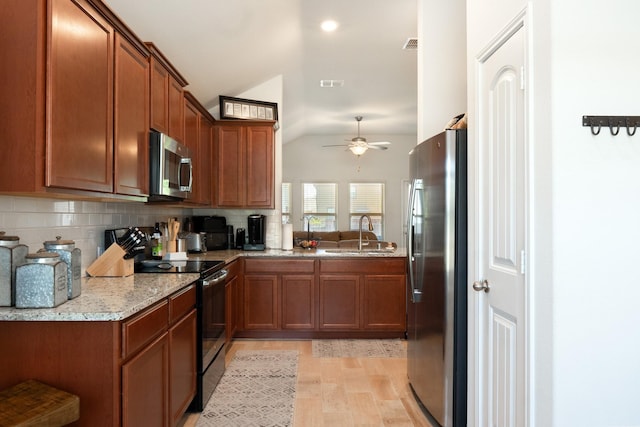 kitchen featuring vaulted ceiling, a sink, brown cabinetry, ceiling fan, and stainless steel appliances