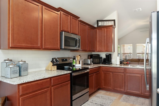 kitchen with lofted ceiling, light wood finished floors, light stone countertops, tasteful backsplash, and appliances with stainless steel finishes