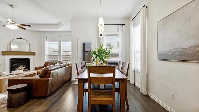 dining space featuring dark wood-style flooring, a ceiling fan, a glass covered fireplace, and baseboards