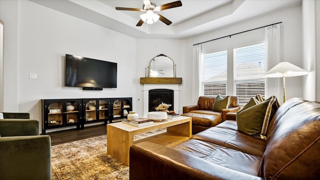 living area with a fireplace, a raised ceiling, wood finished floors, and ceiling fan