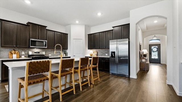 kitchen featuring stainless steel appliances, backsplash, a sink, arched walkways, and dark wood-type flooring