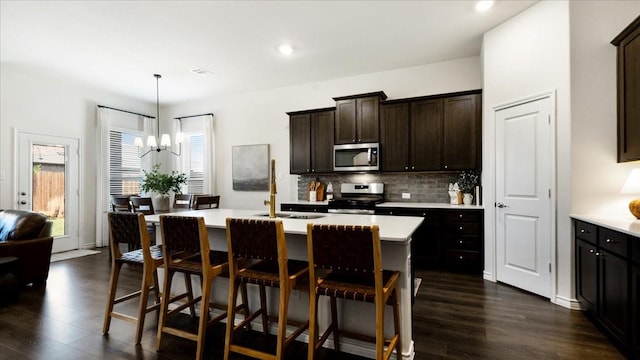 kitchen featuring a sink, an inviting chandelier, stainless steel appliances, backsplash, and dark wood-style flooring