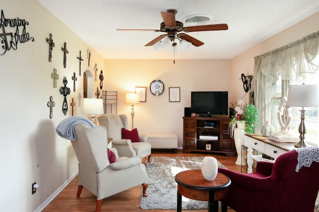 living area featuring visible vents, a ceiling fan, wood finished floors, and a textured ceiling