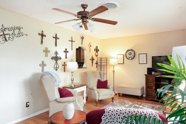 living area featuring arched walkways, a ceiling fan, visible vents, wood finished floors, and baseboards