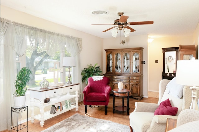 living area featuring wood finished floors, ceiling fan, baseboards, and visible vents