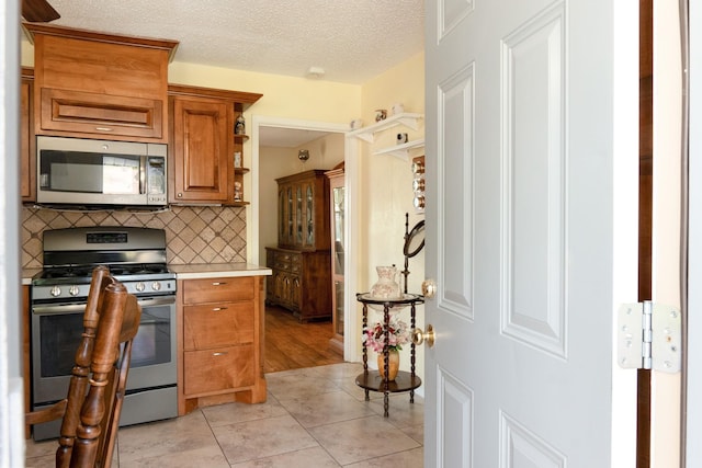 kitchen with light countertops, appliances with stainless steel finishes, a textured ceiling, brown cabinets, and decorative backsplash