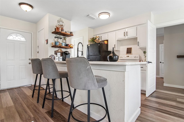 kitchen with dark wood-style flooring, a kitchen breakfast bar, freestanding refrigerator, white cabinets, and visible vents
