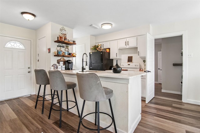 kitchen featuring a peninsula, freestanding refrigerator, a breakfast bar area, dark wood finished floors, and stove