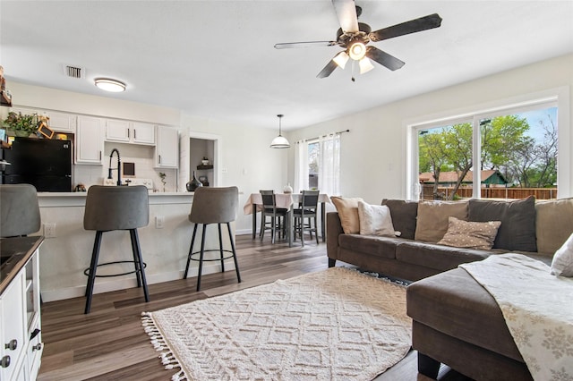 living room with dark wood-type flooring, visible vents, and a ceiling fan