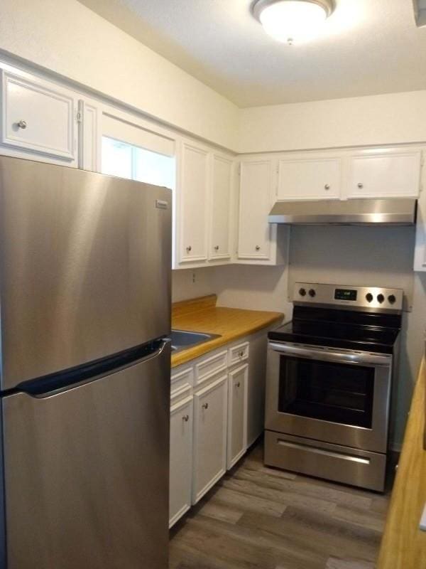 kitchen with dark wood-style floors, white cabinetry, under cabinet range hood, appliances with stainless steel finishes, and a sink