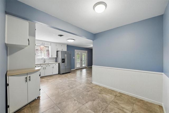 kitchen with stainless steel fridge with ice dispenser, light countertops, a sink, white cabinetry, and french doors